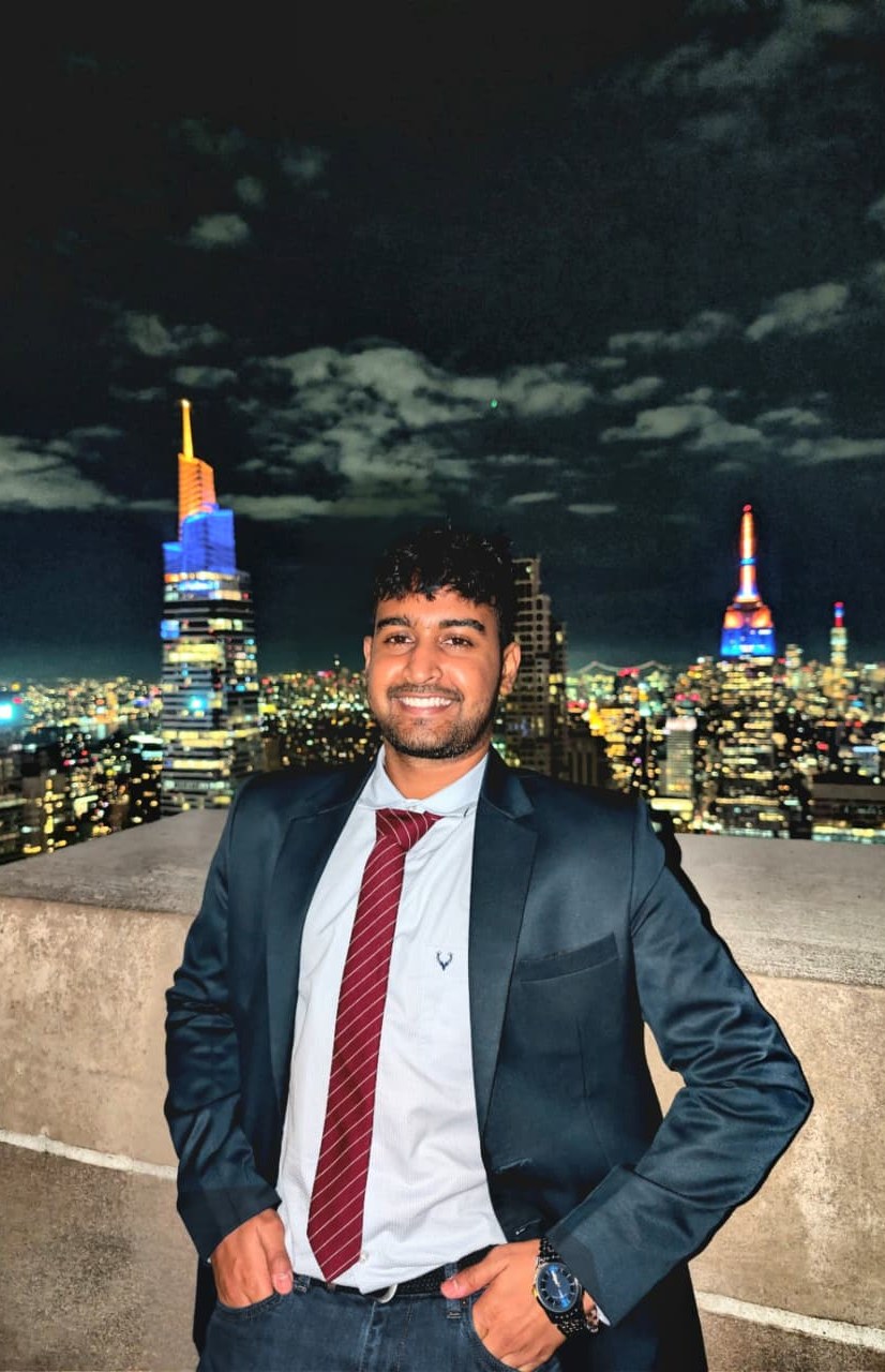 Sri Vasudev on a Manhattan rooftop at night, New York City skyline behind